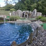 Water fountain in a landscaped park area with rock formations and green turf.