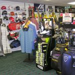 Golf shop display featuring clubs, apparel, and promotional signs for various brands.