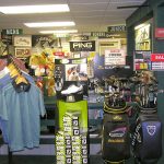 Golf shop interior displaying apparel, clubs, and promotional signs for various brands.
