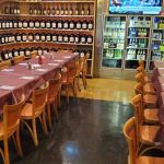 Restaurant interior with long tables set for dining, featuring a well-stocked liquor shelf.