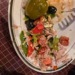 Salad with tuna, tomatoes, olives, and a green pepper on a white plate.