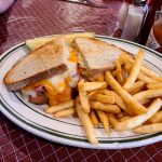 Grilled cheese sandwich and a side of french fries on a white plate.