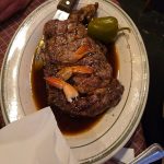 Seared steak with shrimp and a green pepper in a rich brown sauce on a white plate.