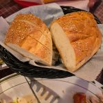 Two loaves of sesame-seed bread on a woven tray, ready to eat.