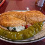 Sandwich served with a large, bright green pepper topping on a white plate.