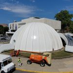 Large white dome structure with construction equipment on a sunny day.