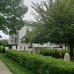 White church with gravestones and green hedges under a cloudy sky.
