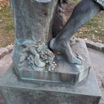 Bronze statue detail showing a sculpted foot resting near carved grapes and foliage on a stone base.