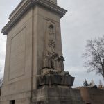 Stone monument with relief sculpture under an overcast sky.
