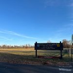Sign at Princeton Battlefield State Park under a bright blue sky with open fields.