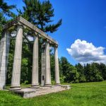 Ancient stone temple ruins under a bright blue sky with white clouds and green trees.