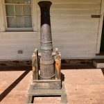 Tall, rusted metal chimney pipe resting on a wooden pallet outside a white building.