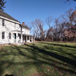White historic farmhouse with porch set on a grassy lawn under a blue sky.