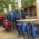 Outdoor display of blue and red life jackets hanging on racks near a wooden structure.
