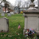 Old gravestones and a large stone monument in a grassy, historic cemetery.