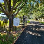 Entrance to Princeton Cemetery with a sign indicating open hours, framed by trees and wrought iron.