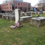 Old cemetery with weathered tombstones and monuments in a grassy urban setting.
