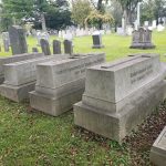 Old stone gravestones in a grassy, historic cemetery under an overcast sky.