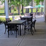 Outdoor patio dining area with tables and chairs under a covered porch overlooking a green lawn.