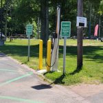 Electric vehicle charging station next to a paved path in a park setting.