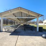 Covered picnic shelter with tables under a blue sky at a park.