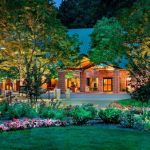 Modern brick building nestled among lush trees and manicured garden at dusk.