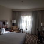 Modern hotel room with large window, bed, and seating area.