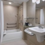Modern bathroom with white tub, shower, and vanity sink in neutral tones.