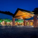 Modern building entrance at night with warm interior lighting under a large overhang.