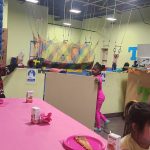 Kids in a colorful gym with hanging nets and a pink table setup.