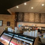 Bakery display case filled with bagels and pastries under a menu board.