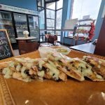 Assortment of drizzled, savory flatbreads on a brown serving tray in a cafe.