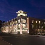 Modern brick building illuminated at night with large windows and streetlights.