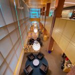 Interior view of a modern bookstore aisle with shelves, seating area, and high ceilings.