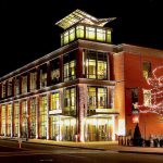 Modern brick building illuminated at night, featuring a glass-enclosed upper section and decorated with holiday lights.