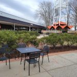 Outdoor seating area in front of a modern building with a clock tower visible in the background.