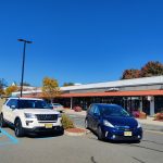 White and blue cars parked in front of a commercial building on a sunny day.