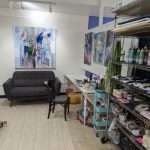Art studio with modern sofa, abstract painting, and shelves of art supplies.