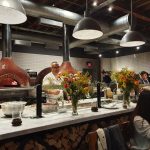 Pizza oven in a modern restaurant with staff cooking and patrons dining at the counter.