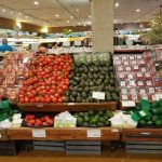 Produce display featuring tomatoes, green vegetables, and other fresh fruits in a grocery store.