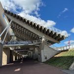 Elevated pedestrian walkway structure against a bright blue, partly cloudy sky.