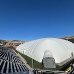 Large white dome structure inside a stadium under a clear blue sky.