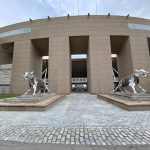 Sculptures of wolves flank the entrance to a modern, circular building.