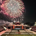 Fireworks explode over a packed football stadium at night during a game.