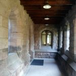 Stone archway hallway with wooden ceiling and arched windows.
