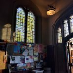 Gothic arched windows overlook a bright, leafy outdoor scene inside a historic building.