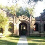 Stone archway entrance to an old, stately building surrounded by greenery.