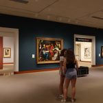 Museum gallery interior with art on walls and visitors viewing paintings.
