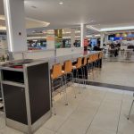 Modern, bright indoor mall food court with seating areas and storefronts.
