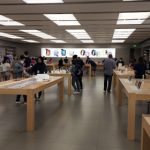 Modern, brightly lit retail space with wooden tables and people browsing displays.